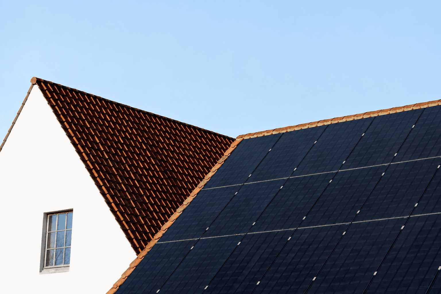 Solar panels installed on a tiled house roof against a clear blue sky